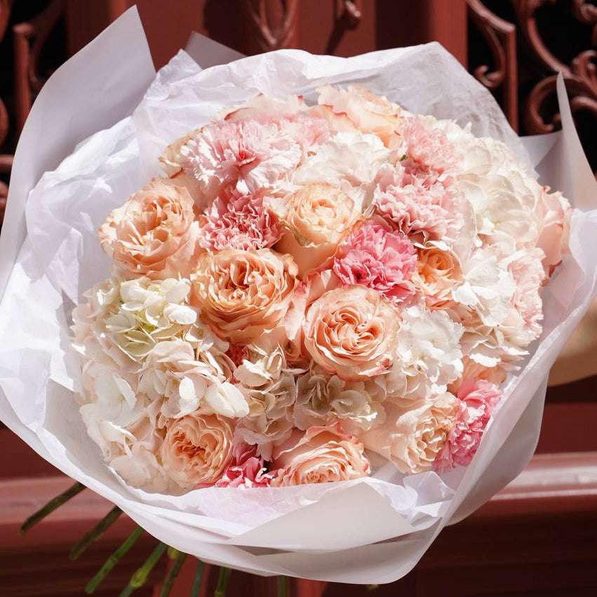 Bouquet of pink and white flowers wrapped in white paper against a decorative brown background