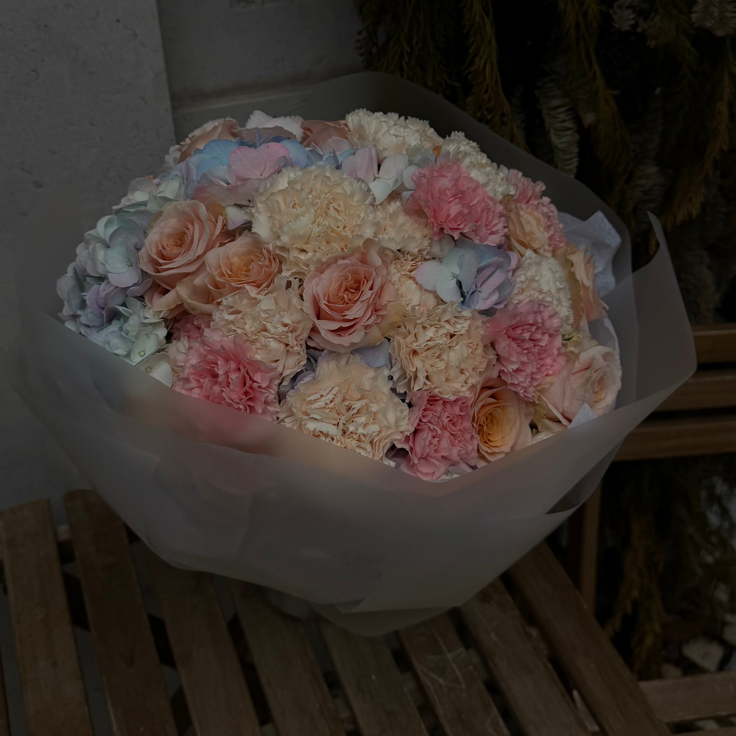 Bouquet of flowers in a box on a wooden surface with a textured wall in the background.