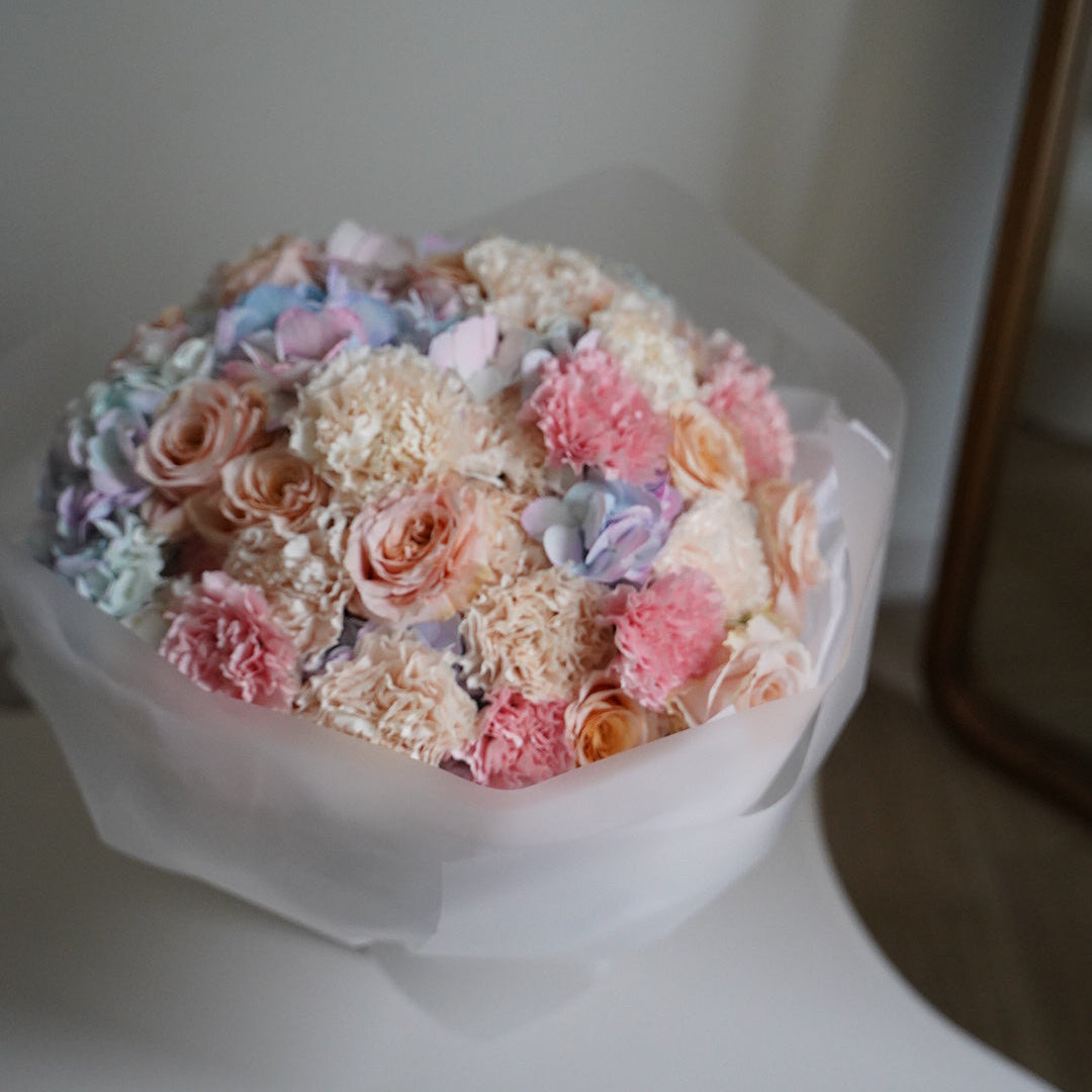 Bouquet of pastel-colored flowers in a clear plastic wrap on a white surface.