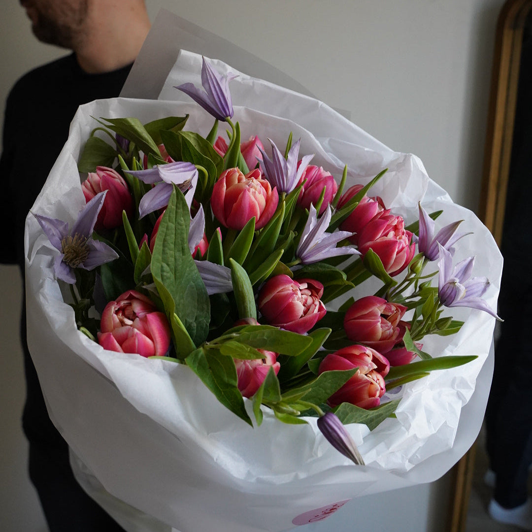 Bouquet of pink and purple tulips wrapped in white paper held by a person.