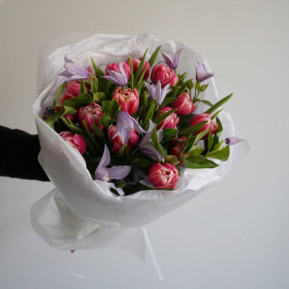 Bouquet of pink tulips wrapped in white paper against a plain background