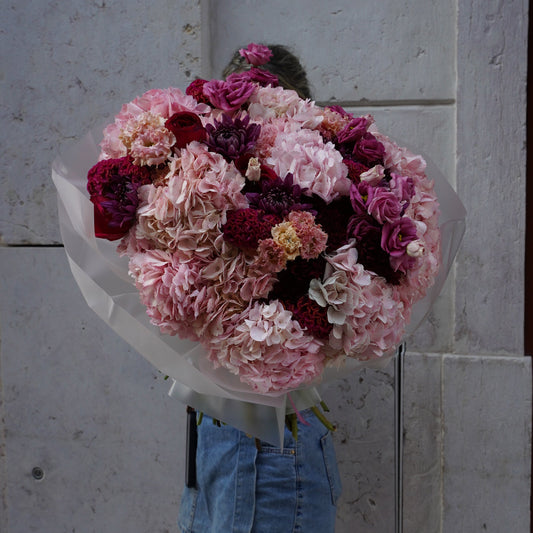 Bouquet of pink and red flowers held by a person wearing denim gloves on a light gray background