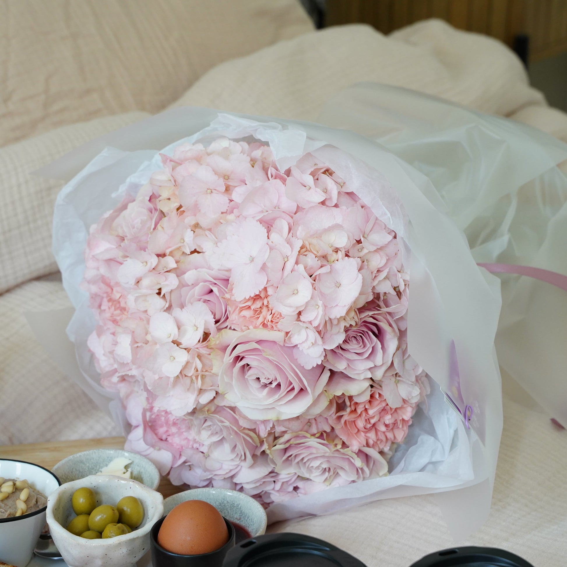 Bouquet of pink flowers on a table with snacks and a coffee cup.