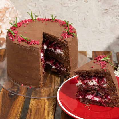 Chocolate cake with a slice taken out, placed on a wooden table with a red plate.