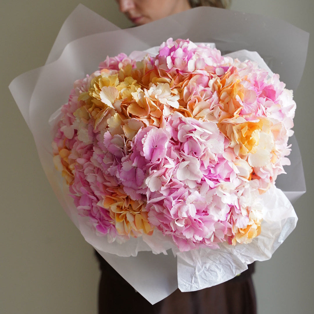 Woman holding a marshmallow hydrangea bouquet with pink and peach flowers, wrapped in white paper
