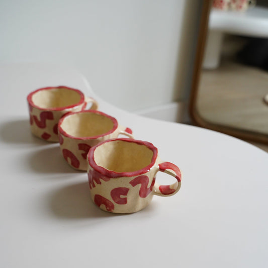 Two decorative cups with red patterns on a white surface